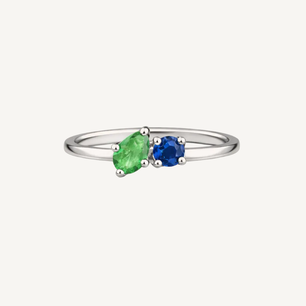Gold ring with green and blue gemstones on a beige background