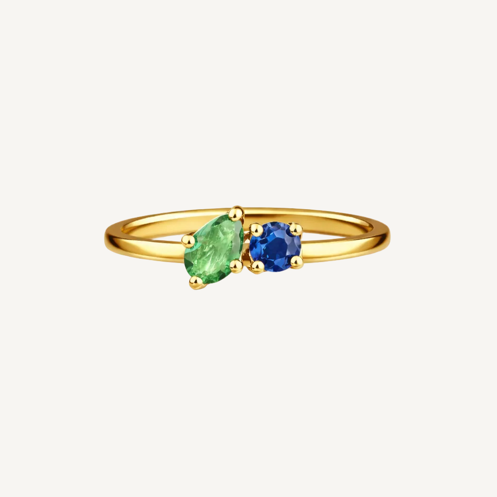 Gold ring with green and blue gemstones on a beige background