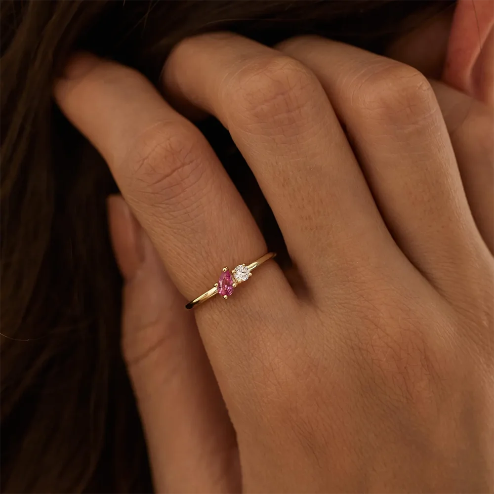 Close-up of a hand wearing a gold ring with pink and white gemstones.