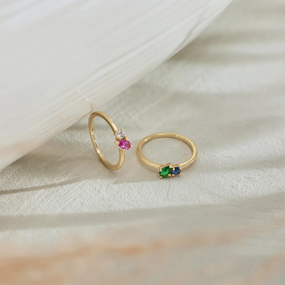 Two gold rings with gemstones on a soft fabric background
