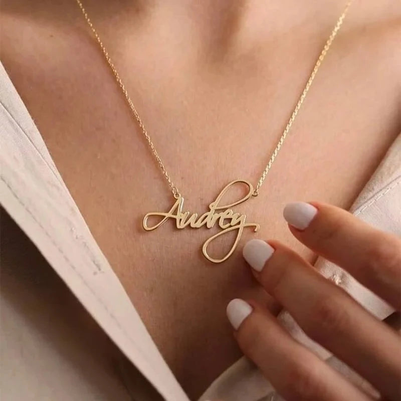 Gold necklace with 'Audrey' pendant on a person wearing a white top.