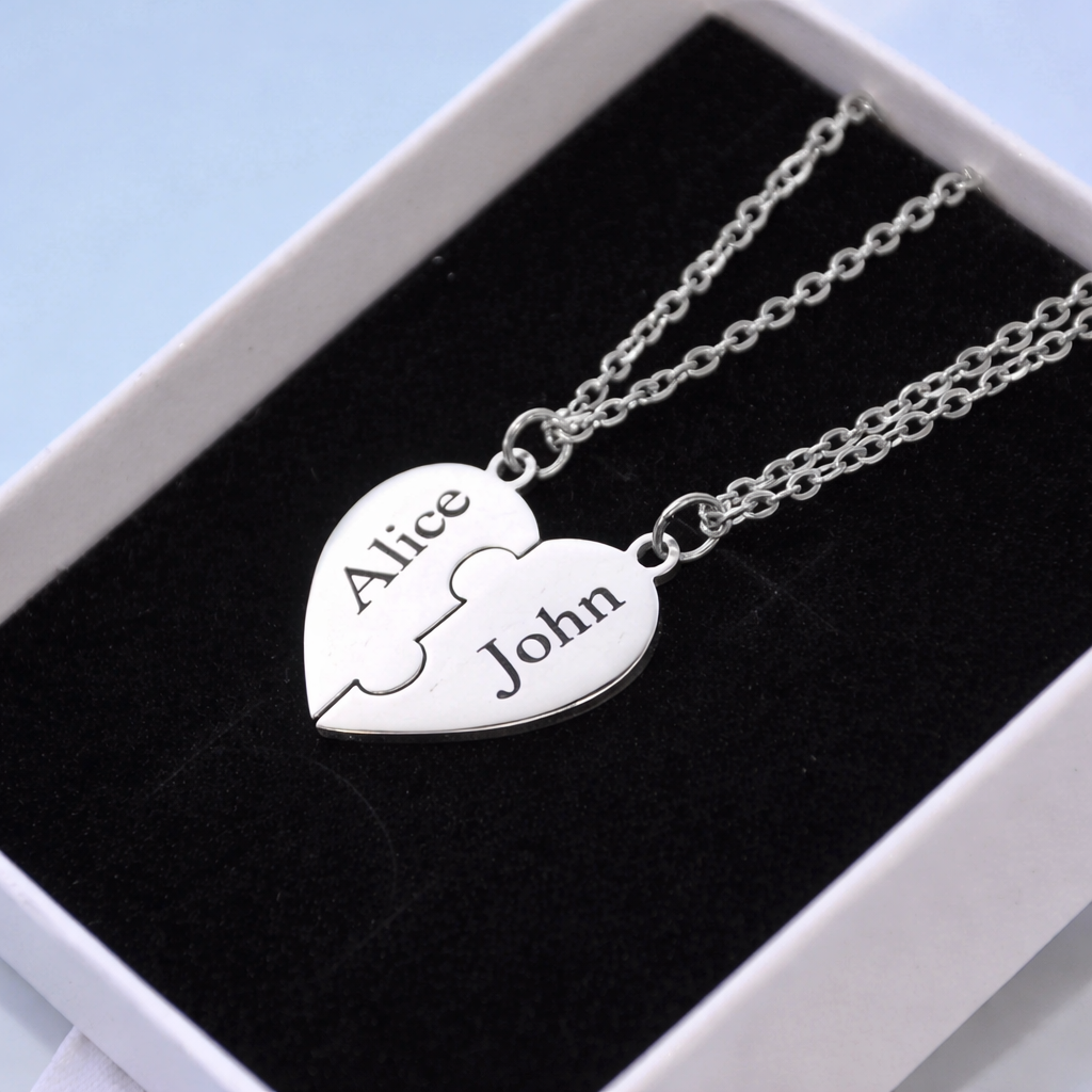 Silver heart-shaped puzzle piece pendant with engraved names on a black cushion in a white box.