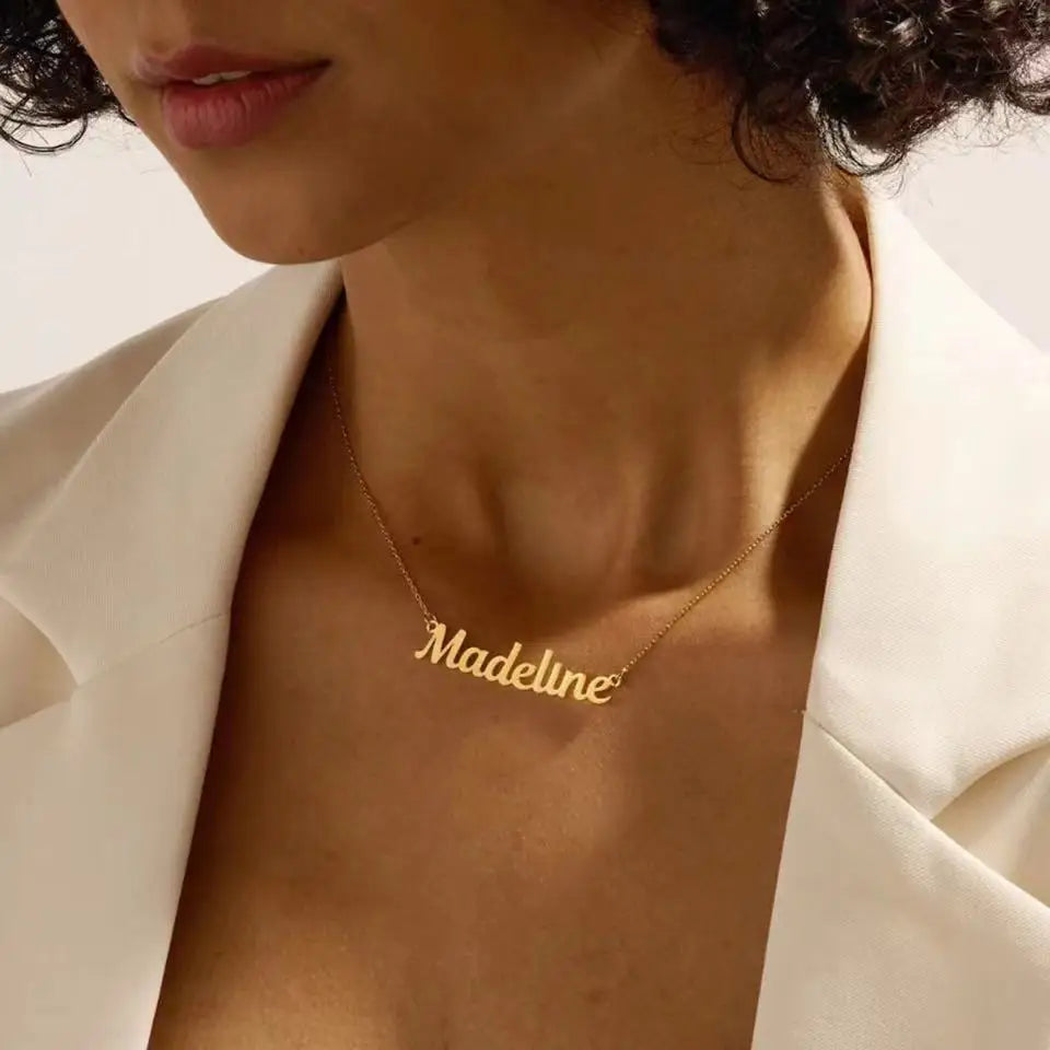 Gold necklace with 'Madeline' pendant on a woman wearing a white blazer.