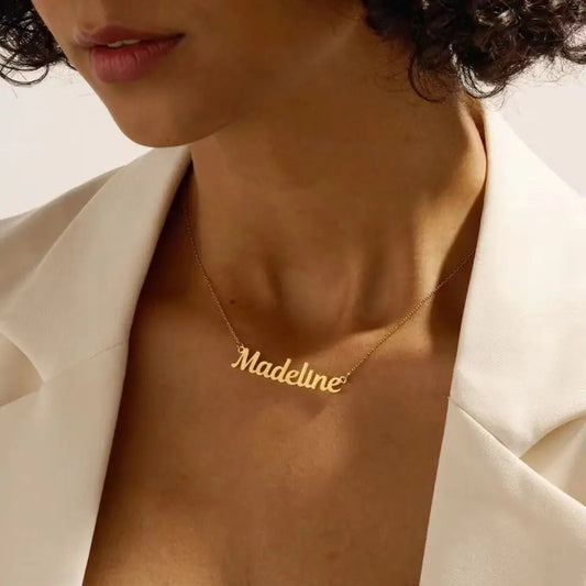Gold necklace with 'Madeline' pendant on a woman wearing a white blazer.